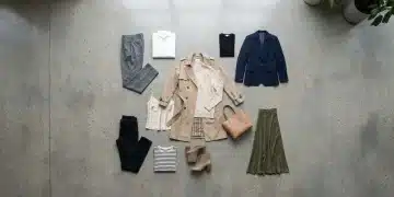 Aerial view of a capsule wardrobe on a concrete floor, featuring a trench coat, cashmere sweater, and silk camisole arranged in a fluid pattern, symbolizing trans-seasonal fashion and adaptable style.