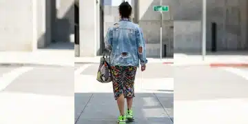 A person walking, viewed from behind, wearing a chaotic outfit of distressed denim, floral print, neon sneakers, and a patterned bag, illustrating common trend-stacking mistakes in outfit inspirations.